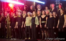 Foto des Chors mit vielen Sängerinnen und Sängern in schwarz-goldener Kleidung