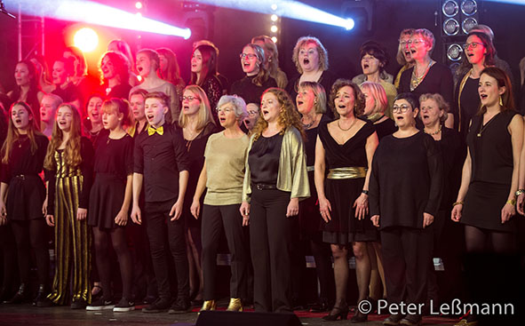 Foto des Chors mit vielen Sängerinnen und Sängern in schwarz-goldener Kleidung